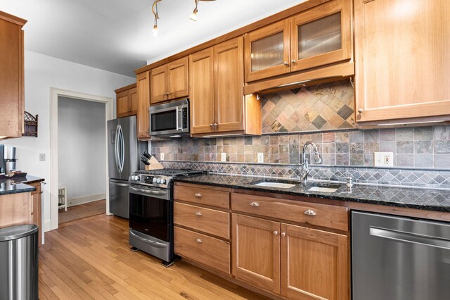 kitchen featuring sink, appliances with stainless steel finishes, dark stone countertops, light wood-type flooring, and decorative backsplash