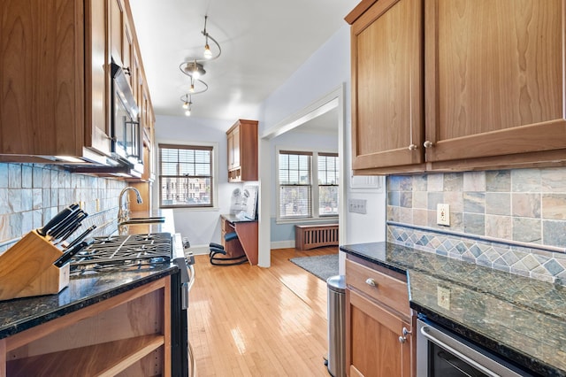 kitchen with light wood-type flooring, sink, radiator heating unit, tasteful backsplash, and black range with gas stovetop