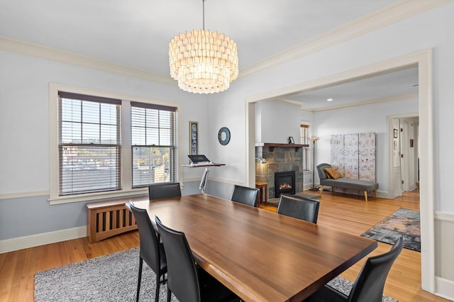 dining space with radiator, a stone fireplace, light hardwood / wood-style flooring, a chandelier, and crown molding