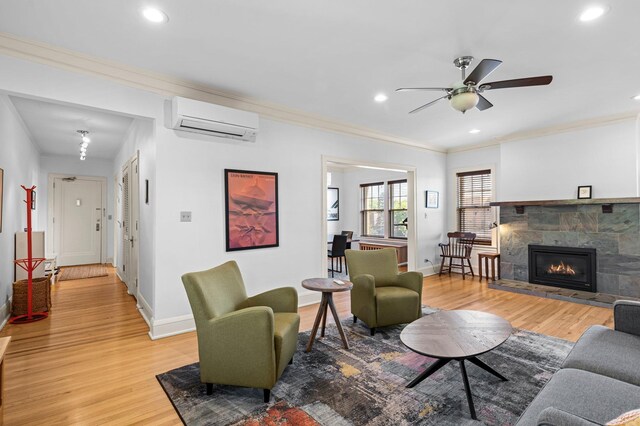 living room with an AC wall unit, a fireplace, light hardwood / wood-style flooring, crown molding, and ceiling fan