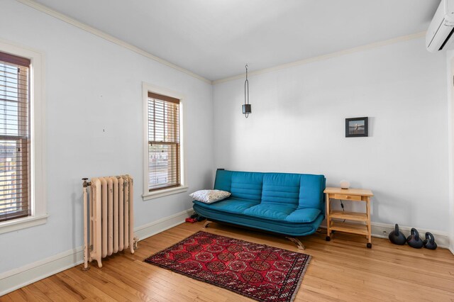 sitting room with a wall unit AC, light hardwood / wood-style floors, radiator heating unit, and a wealth of natural light