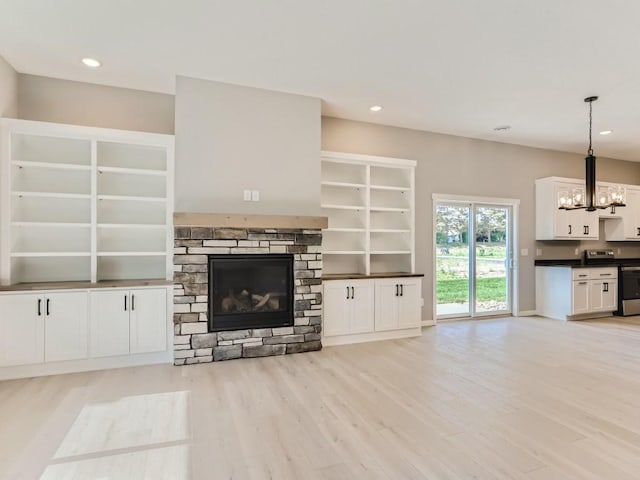 unfurnished living room with a notable chandelier, light wood-type flooring, and a stone fireplace