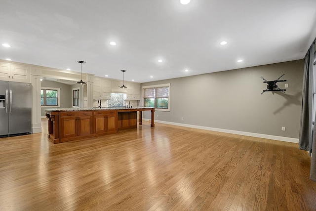 kitchen featuring a large island with sink, a wealth of natural light, decorative light fixtures, and stainless steel refrigerator with ice dispenser