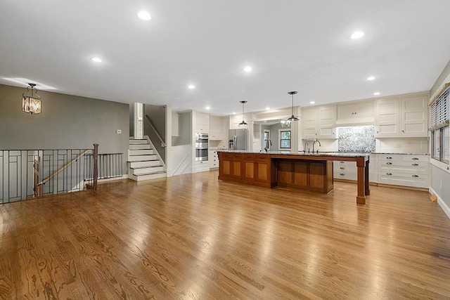 kitchen featuring light hardwood / wood-style floors, a large island with sink, sink, stainless steel appliances, and hanging light fixtures