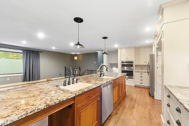 kitchen featuring stainless steel appliances, decorative light fixtures, sink, and light wood-type flooring