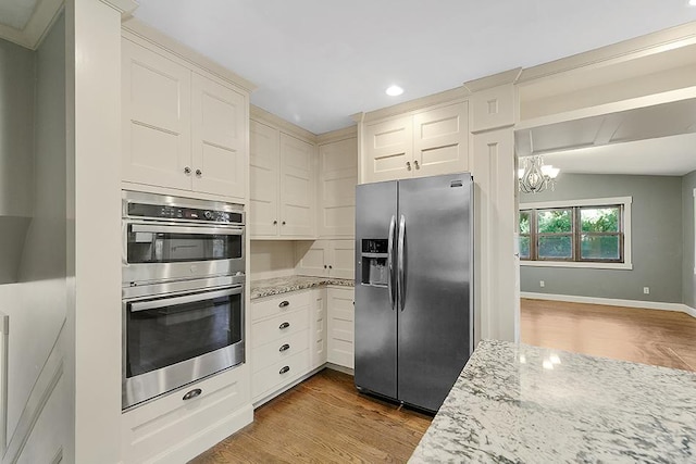 kitchen featuring light stone countertops, light hardwood / wood-style floors, a notable chandelier, vaulted ceiling, and appliances with stainless steel finishes