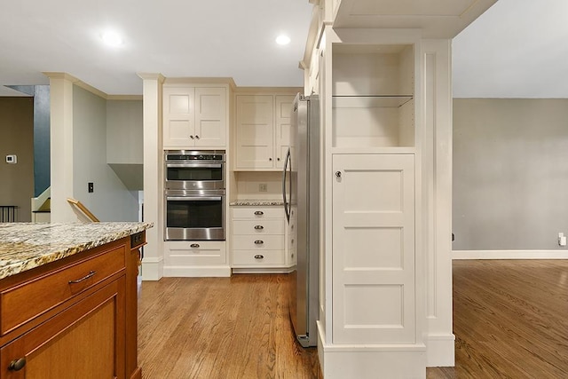 kitchen with white cabinetry, appliances with stainless steel finishes, light stone countertops, light hardwood / wood-style floors, and decorative backsplash