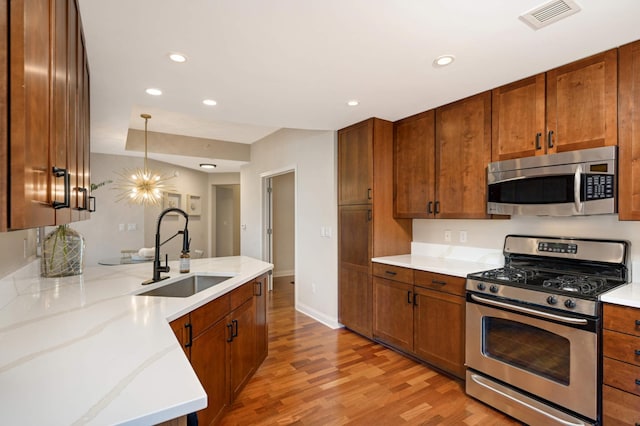 kitchen with pendant lighting, light wood-type flooring, sink, appliances with stainless steel finishes, and light stone countertops