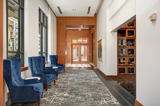 interior space with a towering ceiling, wood walls, dark wood-type flooring, and a healthy amount of sunlight