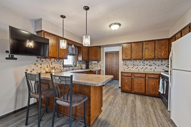 kitchen with a peninsula, brown cabinets, freestanding refrigerator, and black electric range oven