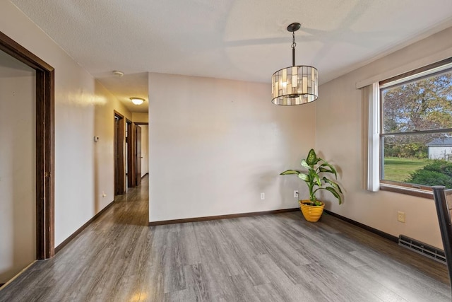 unfurnished room featuring a textured ceiling, wood finished floors, visible vents, baseboards, and an inviting chandelier