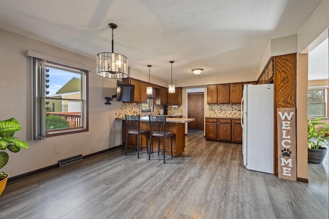 kitchen featuring freestanding refrigerator, visible vents, a peninsula, and decorative backsplash