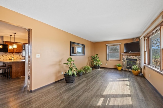 unfurnished living room featuring dark wood-style floors, baseboards, an inviting chandelier, and a stone fireplace