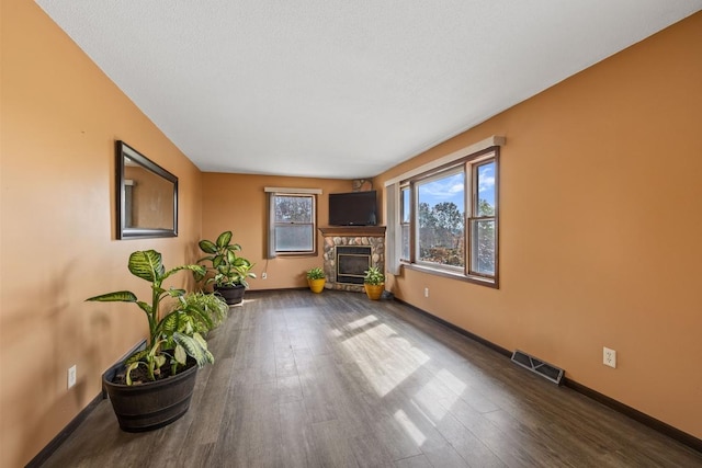 unfurnished living room featuring wood finished floors, a glass covered fireplace, visible vents, and baseboards