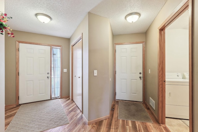 foyer featuring light wood-type flooring, washer / clothes dryer, and a textured ceiling