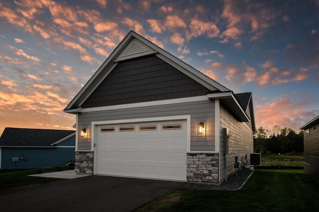 property exterior at dusk with a lawn, cooling unit, and a garage