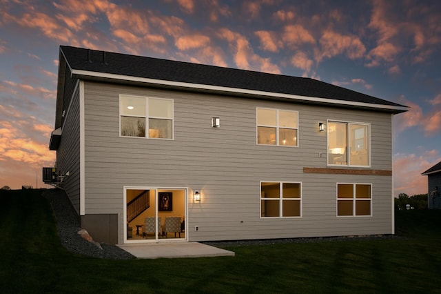 back house at dusk with a yard, a patio area, and central air condition unit