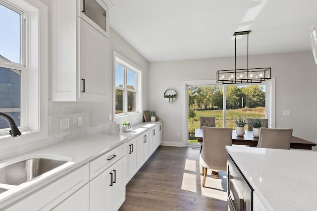 kitchen with light stone counters, white cabinetry, dark hardwood / wood-style floors, and hanging light fixtures