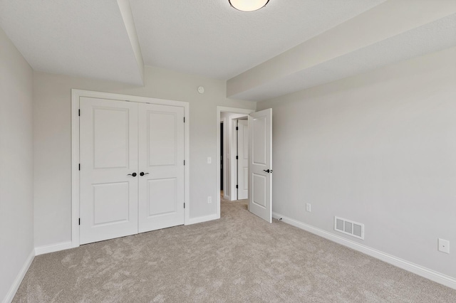 unfurnished bedroom with light colored carpet and a closet