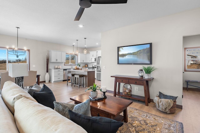 living room with ceiling fan with notable chandelier and light wood-type flooring