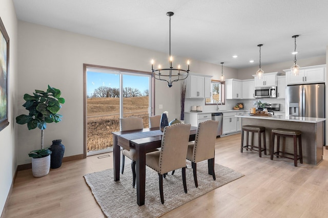 dining room with light wood-type flooring, a chandelier, sink, and a wealth of natural light