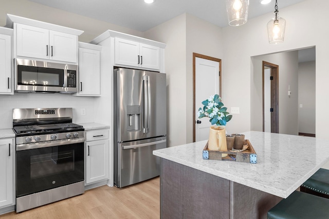 kitchen with stainless steel appliances, white cabinetry, pendant lighting, and light wood-type flooring