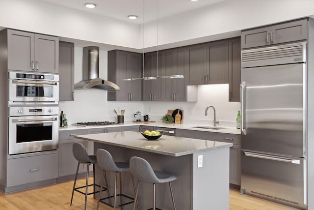 kitchen featuring appliances with stainless steel finishes, sink, wall chimney range hood, light hardwood / wood-style floors, and a kitchen island