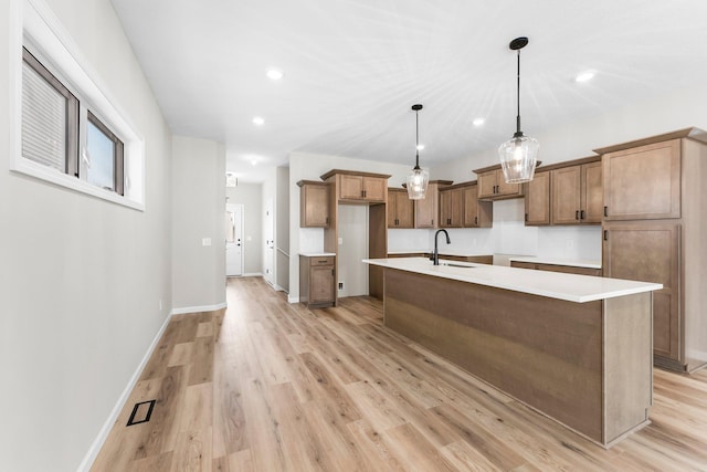 kitchen featuring sink, a center island with sink, pendant lighting, and light wood-type flooring