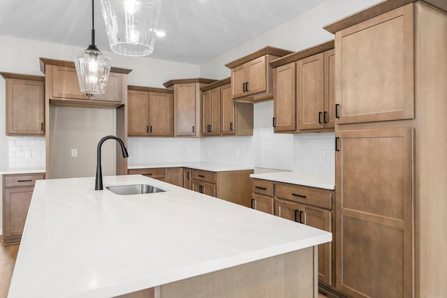 kitchen with pendant lighting, a kitchen island with sink, sink, a textured ceiling, and tasteful backsplash