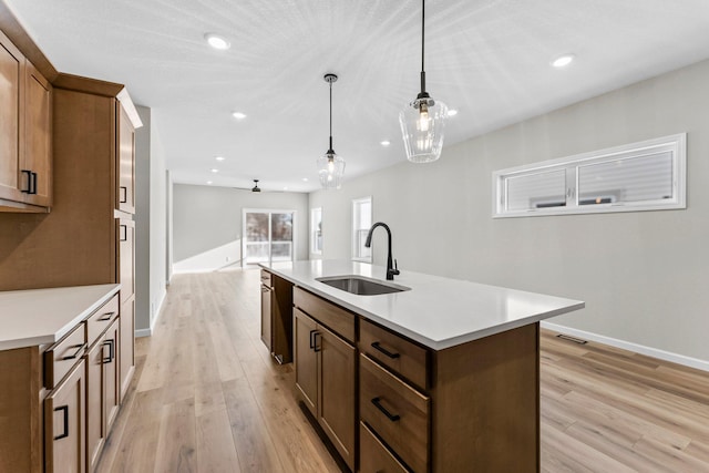 kitchen with a kitchen island with sink, hanging light fixtures, sink, ceiling fan, and light wood-type flooring