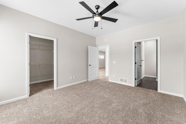 unfurnished bedroom featuring carpet flooring, ceiling fan, a walk in closet, and a closet