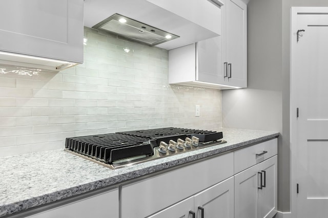 kitchen with backsplash, wall chimney range hood, light stone counters, white cabinetry, and stainless steel gas cooktop