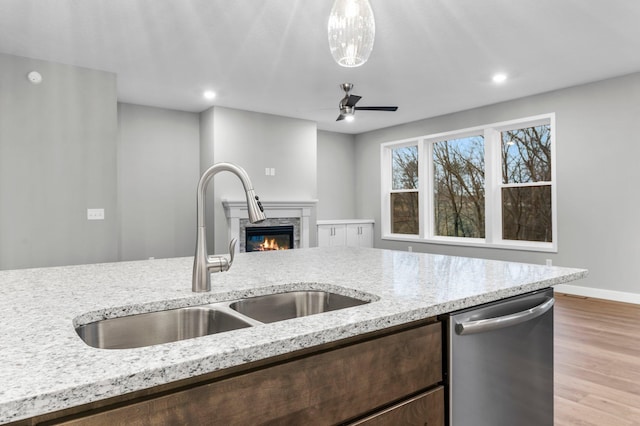 kitchen with dishwasher, sink, light hardwood / wood-style flooring, ceiling fan, and light stone countertops