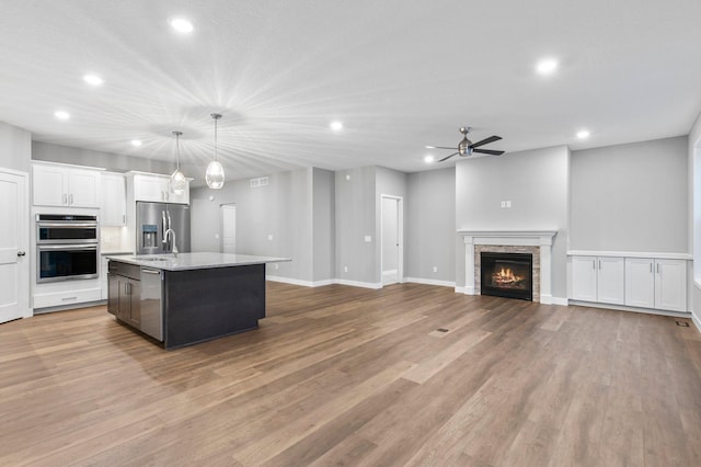 kitchen with stainless steel appliances, a center island with sink, a fireplace, hardwood / wood-style floors, and hanging light fixtures