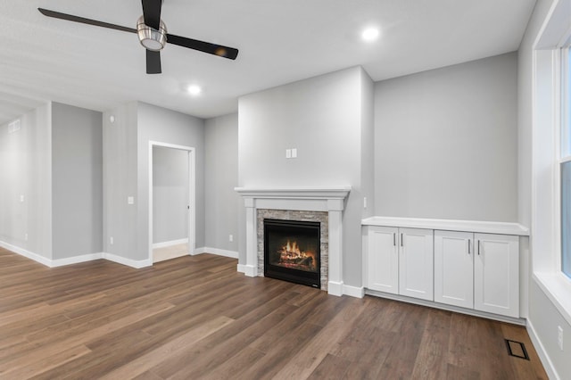 unfurnished living room featuring dark hardwood / wood-style floors, ceiling fan, and a stone fireplace