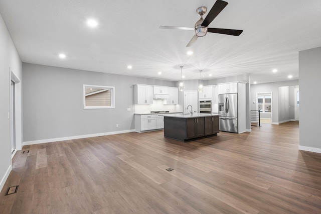 kitchen featuring a kitchen island with sink, hanging light fixtures, sink, stainless steel refrigerator with ice dispenser, and hardwood / wood-style flooring