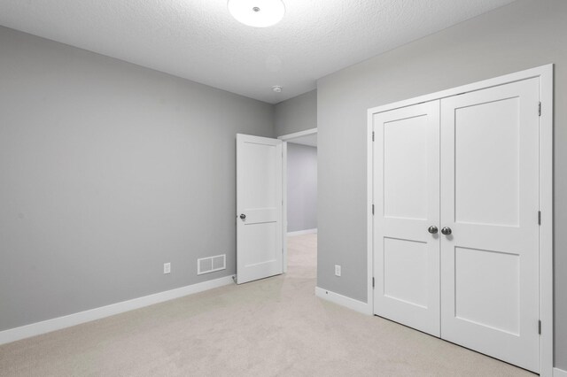 unfurnished bedroom featuring light carpet, a textured ceiling, and a closet