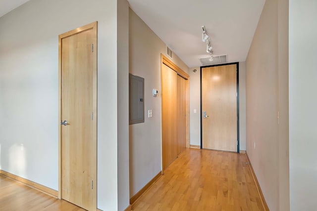 corridor featuring rail lighting, electric panel, and light wood-type flooring