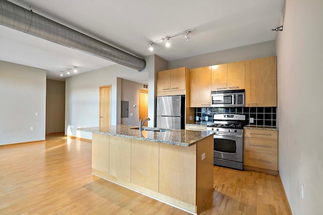 kitchen with stone counters, stainless steel appliances, tasteful backsplash, light hardwood / wood-style floors, and a center island with sink