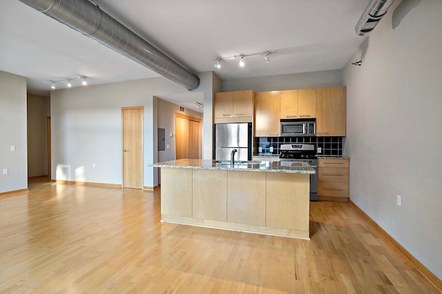 kitchen with stainless steel appliances, light stone countertops, a center island with sink, and light hardwood / wood-style floors