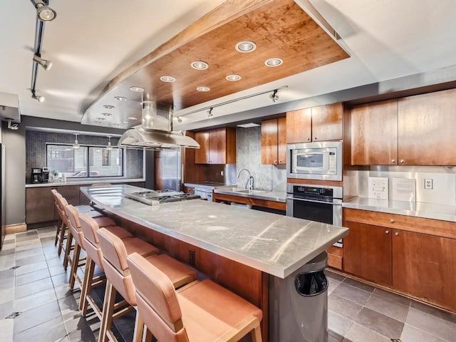 kitchen with stainless steel appliances, brown cabinetry, a spacious island, and island range hood