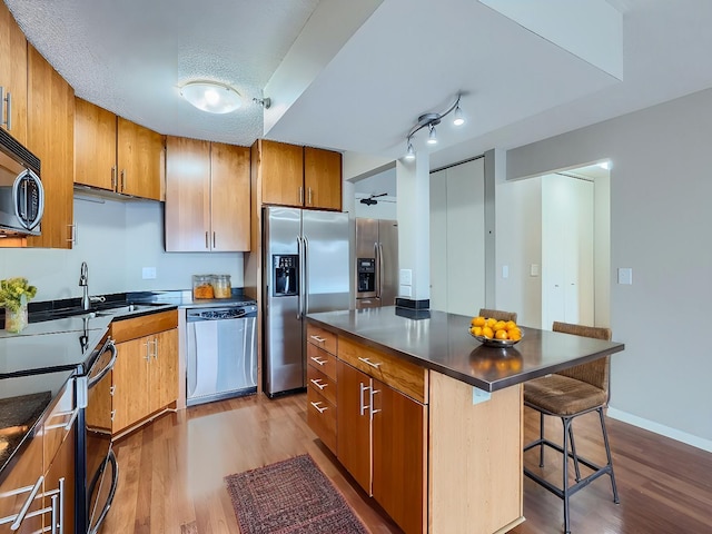 kitchen featuring stainless steel appliances, dark countertops, brown cabinets, and light wood-style flooring