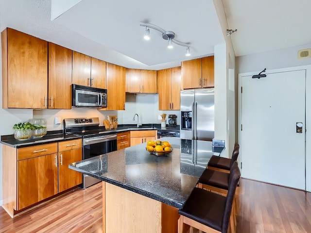 kitchen featuring appliances with stainless steel finishes, brown cabinets, a breakfast bar area, light wood-style floors, and a sink