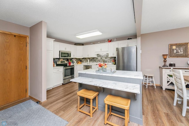 kitchen with light hardwood / wood-style floors, white cabinetry, a kitchen bar, a kitchen island, and stainless steel appliances