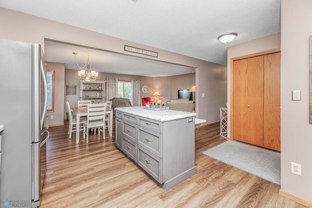 kitchen featuring stainless steel fridge, pendant lighting, gray cabinets, light wood-type flooring, and an inviting chandelier