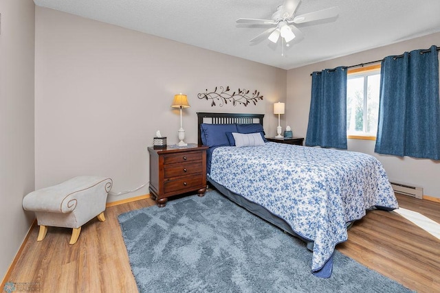 bedroom with a baseboard heating unit, ceiling fan, and wood-type flooring