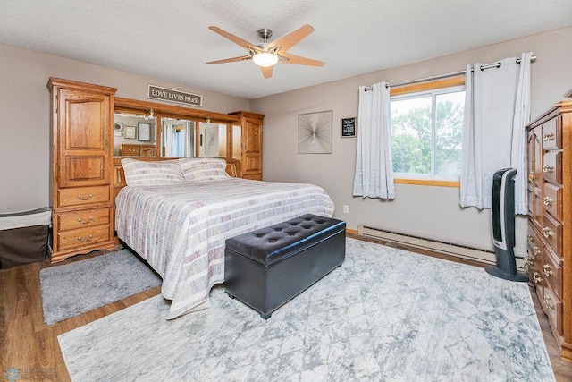 bedroom featuring ceiling fan, a textured ceiling, light hardwood / wood-style flooring, and a baseboard heating unit