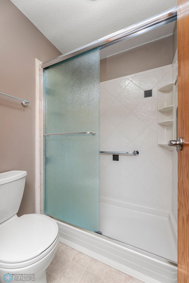 bathroom with a textured ceiling, tile patterned flooring, toilet, and a shower with shower door