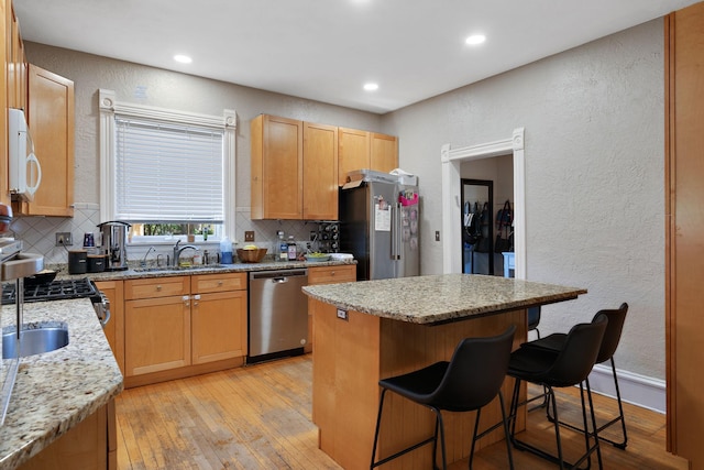 kitchen featuring light stone countertops, stainless steel appliances, light hardwood / wood-style floors, and a kitchen island