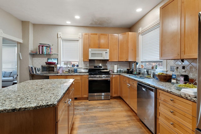 kitchen featuring appliances with stainless steel finishes, light hardwood / wood-style floors, light stone counters, tasteful backsplash, and sink